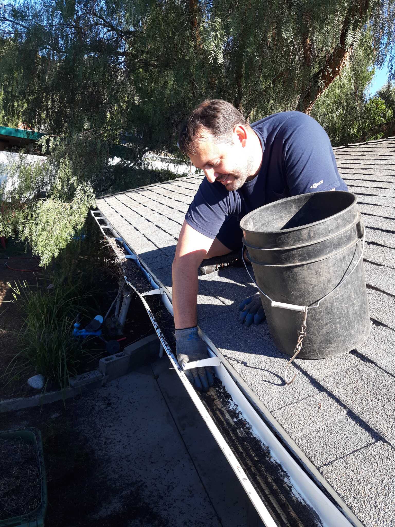 Technician cleaning a rain gutter and clearing roof debris